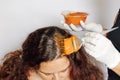 Woman with coloring brush in one hand and hair dye bowl in the other applying red substance on woman hair roots. Hair Royalty Free Stock Photo