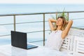 A woman combines rest and remote work in a summer cafe against the background of the sea, the concept of freedom and independence