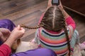 Braiding pigtails close up. A little girl plays on her phone while her mother does her hair. A woman braids a little girl`s hair. Royalty Free Stock Photo