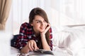 Woman is comfortable lying on her bed with a book, smiling and happy and dreaming