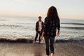 Woman coming to boyfriend that standing in the water on the seashore, young couple meeting sunrise on the sea together
