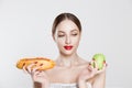 Woman compare tasty unhealthy burger sandwich hotdog in hand and green apple getting ready to eat healthy food isolated on a white Royalty Free Stock Photo