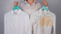 A woman compares two white shirts before and after washing. The girl is holding one blouse, clean and ironed, and the Royalty Free Stock Photo