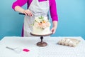 Woman confectioner pastry-cook decorate appetizing creamy white two-tiered wedding cake decorated with fresh flowers on Royalty Free Stock Photo