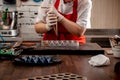 A woman confectioner with red uniform and white sterile gloves do a set of colorful chocolates from milk chocolate on a