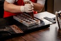 A woman confectioner with red uniform and white sterile gloves do a set of colorful chocolates from milk chocolate on a