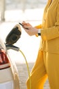 Woman connects an electric car to the charger and adjusts the process of charging the car battery using a cell phone Royalty Free Stock Photo