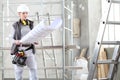 Woman construction worker builder looking at bluprint, wearing helmet, hearing protection headphones and tools belt bag in Royalty Free Stock Photo