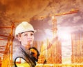 Woman construction worker on building site with crane with safety hard hat and hearing protection headphones, double exposure sky