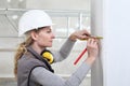 Woman construction worker work with meter tape and pencil, measure wall in interior building site, wearing helmet and hearing Royalty Free Stock Photo