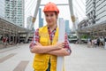 Woman constructor in safety vest with helmet crossed arms and holding construction site layout in the urban