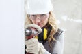 Woman contruction worker using cordless drill driver making a hole in wall, builder with safety hard hat, hearing protection Royalty Free Stock Photo