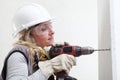 Woman contruction worker using cordless drill driver making a hole in wall, builder with safety hard hat, hearing protection Royalty Free Stock Photo