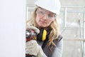 Woman contruction worker using cordless drill driver making a hole in wall, builder with safety hard hat, hearing protection Royalty Free Stock Photo