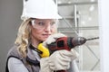 Woman contruction worker using cordless drill driver making a hole in wall, builder with safety hard hat, hearing protection Royalty Free Stock Photo