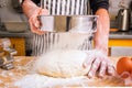 Woman cook in a home kitchen vigorously sprinkles flour on a dough lying on the kitchen table through a sieve. White flour flies i