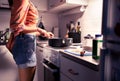 Woman cooking dinner in home kitchen at night. Healthy vegan or vegetarian diet. Stir food in frying pan on stove. Royalty Free Stock Photo