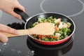 Woman cooking frozen vegetable mix on induction stove, closeup