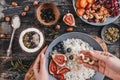 Woman cooking Rice coconut porridge with figs, berries, nuts and coconut milk in plate on rustic wooden background.