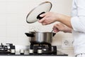 Woman is cooking soup in kitchen. housewife prepares food at home. caucasian woman holds lid from saucepan in her hand