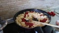 Woman cooking tomato pasta in a frying pan, putting on ketchup and stirs up