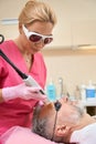 Woman cosmetologist in glasses performs laser hair removal to man