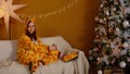 Woman in costume of giraffe sitting on couchon Christmas eve. Smiling young woman in funny pyjamas of giraffe sitting on Royalty Free Stock Photo