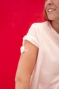 Woman With Cotton Wool Taped To Arm After Injection Or Vaccination Against Red Background