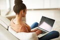 Woman on couch with laptop, typing for blog and freelance copywriter working from home. Female freelancer in living room