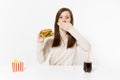 Woman cover mouth with hand at table with burger, french fries, cola in glass bottle isolated on white background Royalty Free Stock Photo