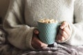 Woman covered with blanket holding mug of hot drink with whipped cream