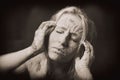 Woman covered in dry cracked clay mask holding her head