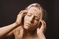 Woman covered in dry cracked clay mud mask holding her head Royalty Free Stock Photo