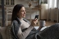 Woman covered with plaid hold teacup, smartphone relaxing at home Royalty Free Stock Photo