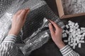 Woman covering silver candlesticks with bubble wrap at dark grey table, closeup