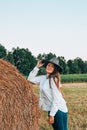 Woman in cowboy hat staying near a straw bale. Summer, beauty, fashion, glamour, lifestyle concept. Cottagecore farmcore Royalty Free Stock Photo