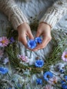 Woman in cozy gray sweater making a wreath of fresh wild flowers and herbs for midsummer celebration. Generative AI Royalty Free Stock Photo