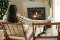 Woman in cozy sweater relaxing with cute cat together and looking at fireplace with festive mantle on background of stylish Royalty Free Stock Photo