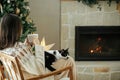 Woman in cozy sweater sitting with cute cat and warm tea on background of fireplace and stylish decorated christmas tree. Owner Royalty Free Stock Photo