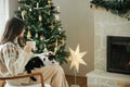 Woman in cozy sweater sitting with cute cat and warm tea on background of fireplace and stylish decorated christmas tree. Owner Royalty Free Stock Photo