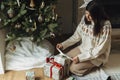 Woman in cozy sweater wrapping stylish christmas gifts under decorated christmas tree with modern vintage baubles. Atmospheric Royalty Free Stock Photo