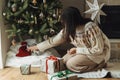 Woman in cozy sweater wrapping stylish christmas gifts under decorated christmas tree with modern vintage baubles. Atmospheric Royalty Free Stock Photo