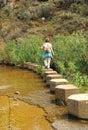 Woman crossing a stream on concrete piles, hiking in the Sierra Norte de Sevilla Natural Park, Spain