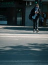 Woman crossing the street while looking at her smartphone. Woman wearing a face mask with green traffic light behind her