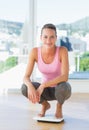 Woman crouching on weighing scale in gym Royalty Free Stock Photo