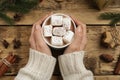 Woman with cup of delicious marshmallow cocoa at wooden table, top view