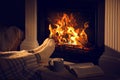 Woman with cup of drink and book near fireplace at home, closeup Royalty Free Stock Photo