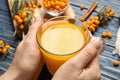 Woman with cup of fresh sea buckthorn tea at blue wooden table, closeup Royalty Free Stock Photo