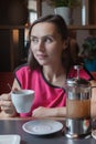 A woman with a cup in hand sits in a cafe and looks away. Royalty Free Stock Photo