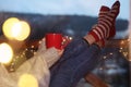 Woman with cup of hot beverage and Christmas lights resting on balcony. Winter